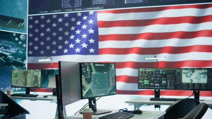 A command center with multiple computer monitors and an American flag in the background