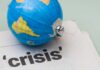 A small globe resting on a newspaper with the word 'crisis'