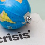 A small globe resting on a newspaper with the word 'crisis'