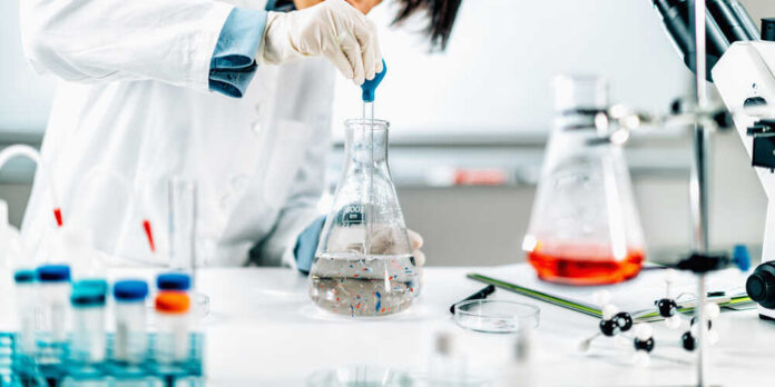 shutterstock_1924877150.jpg Scientist in a lab using a pipette to transfer liquid into a flask