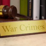 A wooden gavel next to a nameplate reading 'War Crimes'