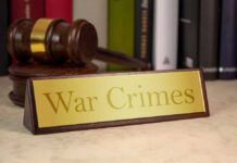 A wooden gavel next to a nameplate reading 'War Crimes'