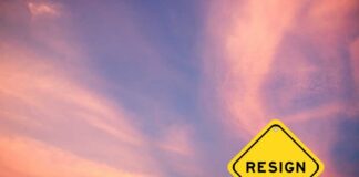 A yellow warning sign with the word 'RESIGN' against a colorful sunset sky