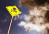 A yellow warning sign with a skull and crossbones against a cloudy sky