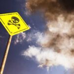 A yellow warning sign with a skull and crossbones against a cloudy sky