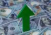 Green arrow pointing upwards on a background of hundred dollar bills