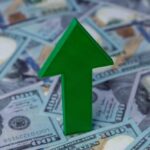 Green arrow pointing upwards on a background of hundred dollar bills