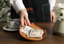 A hand placing cash and a receipt on a wooden plate next to a cup of coffee