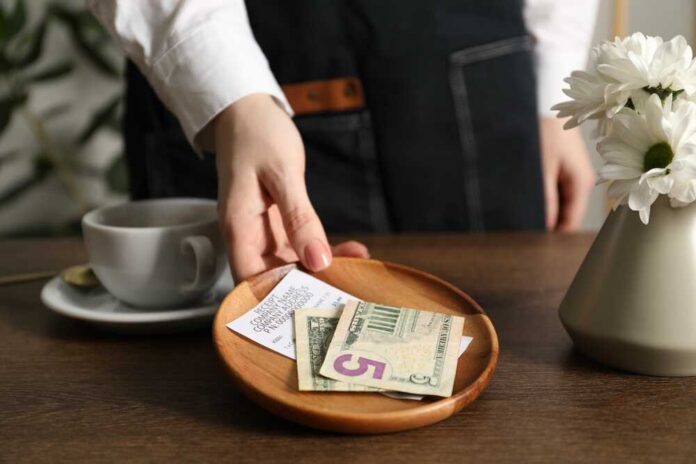 A hand placing cash and a receipt on a wooden plate next to a cup of coffee
