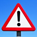 A triangular warning sign with an exclamation mark against a blue sky