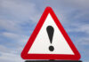 A triangular warning sign with an exclamation mark against a blue sky