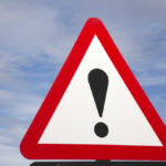 A triangular warning sign with an exclamation mark against a blue sky