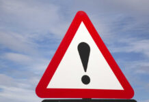 A triangular warning sign with an exclamation mark against a blue sky