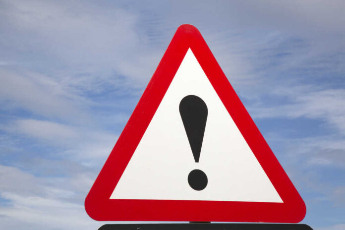 A triangular warning sign with an exclamation mark against a blue sky