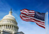 January 6 Attackers May Get Millions? U.S. Capitol building with American flag waving.