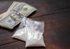 Bundles of cash next to bags of white powder on a wooden surface
