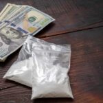 Bundles of cash next to bags of white powder on a wooden surface