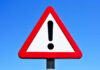 Fatal Umbrella Strike – Really? A triangular warning sign with an exclamation mark against a blue sky