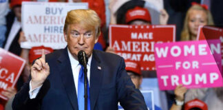 Man speaking at podium with various political signs behind.