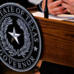 DEXIT Wave Slams Delaware – Texas Wins Seal of Texas Governor on wooden podium.