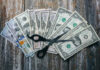 Trump Threat: States Could Lose Cash Because of THIS! Scissors placed on a spread of various U.S. dollar bills
