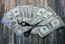 Trump Threat: States Could Lose Cash Because of THIS! Scissors placed on a spread of various U.S. dollar bills
