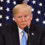 Donald Trump speaking with American flags in background.
