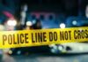Police line caution tape at a crime scene with blurred figures in the background
