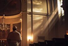 A clergy member standing in a church with light streaming through windows