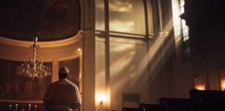 A clergy member standing in a church with light streaming through windows