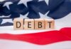Debt Bomb Ticks — 2008 Vibes Return Wooden blocks spelling 'DEBT' on an American flag background