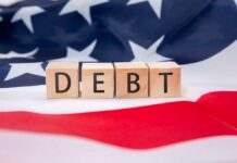 Debt Bomb Ticks — 2008 Vibes Return Wooden blocks spelling 'DEBT' on an American flag background