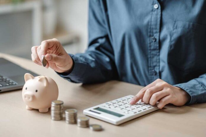 Person placing a coin into a piggy bank while using a calculator