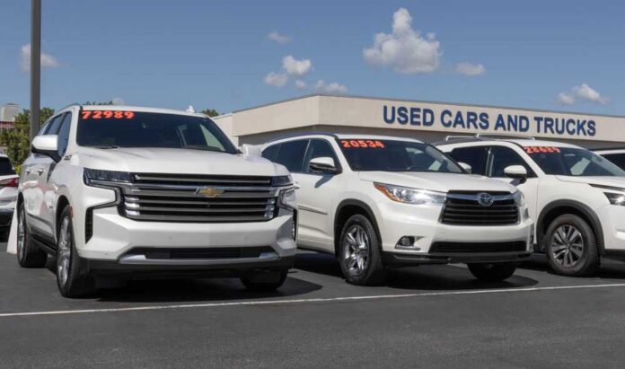 Two white SUVs parked at a used car dealership with price tags visible