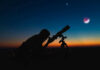 Tiny Planet Exposes Cosmic Carve-Out Silhouette of person using telescope against colorful twilight sky.