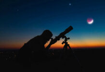 Tiny Planet Exposes Cosmic Carve-Out Silhouette of person using telescope against colorful twilight sky.