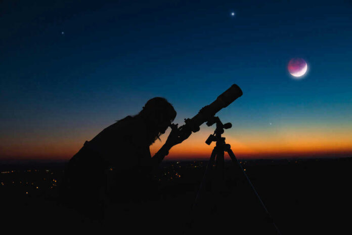 shutterstock_1715179471 Silhouette of person using telescope against colorful twilight sky.