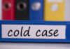 Buried Under Garage — Name Finally Revealed Blue binder labeled 'cold case' with other colored binders in the background