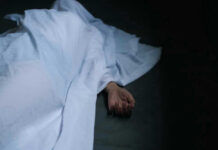 Hand emerging from under white sheet on dark surface.