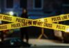 Body In School Chimney — Police Stumped Police tape marking a crime scene with blurred figures in the background