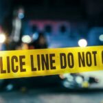 Police line caution tape at a crime scene with blurred figures in the background