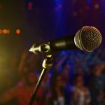 Beloved Singing Icon Vanishes — Now We Know Why Close-up of a microphone in front of a blurred audience at a concert