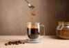 Spoon sprinkling instant coffee granules into a glass cup