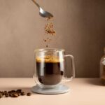 Spoon sprinkling instant coffee granules into a glass cup