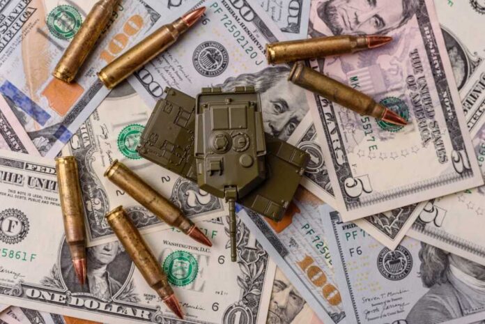Money,,Cash,Dollars,To,Fund,Weapons,For,War,And,Defense A toy military vehicle surrounded by bullets and U.S. dollar bills