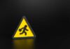 Workers Vanish — Markets Cheer Anyway Yellow triangular warning sign with walking figure and briefcase on black background