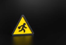 Workers Vanish — Markets Cheer Anyway Yellow triangular warning sign with walking figure and briefcase on black background
