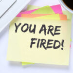 Microsoft Axes 4,800 — Not AI? A sticky note with the message 'YOU ARE FIRED!' placed on a desk next to a keyboard and a cup of coffee