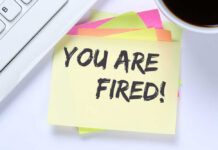 Microsoft Axes 4,800 — Not AI? A sticky note with the message 'YOU ARE FIRED!' placed on a desk next to a keyboard and a cup of coffee
