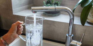 Hand filling pitcher with water from faucet.